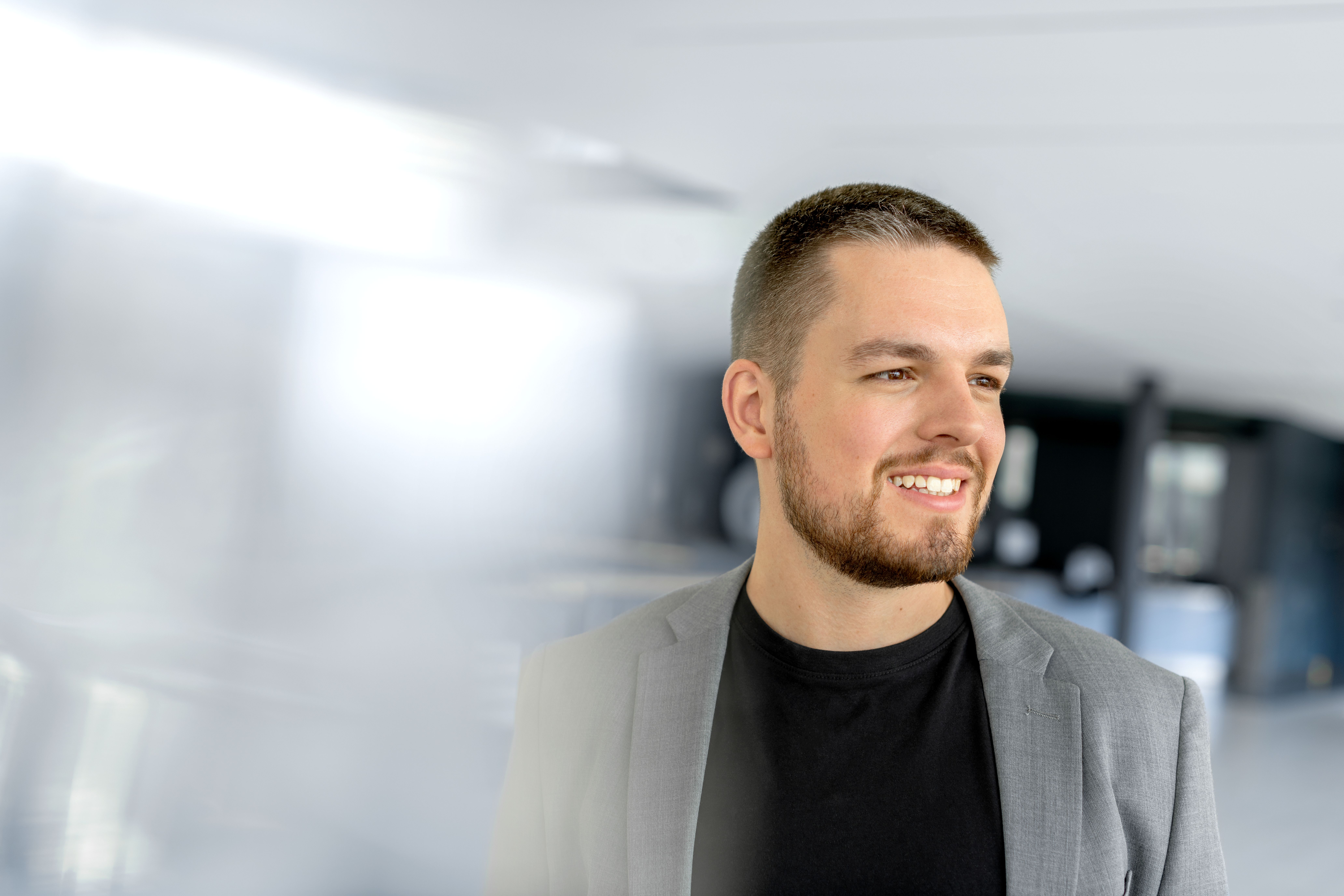 A man wearing a suit is smiling to the right side.