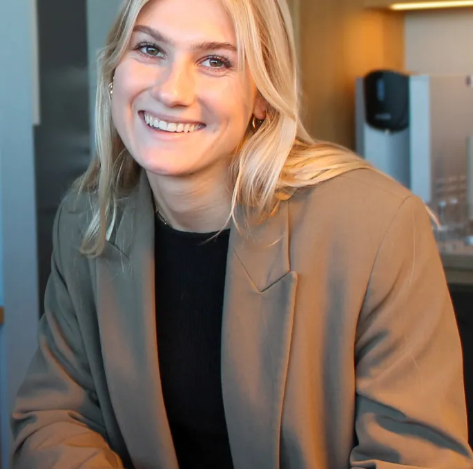 A woman is sitting at a table and is drinking coffee.