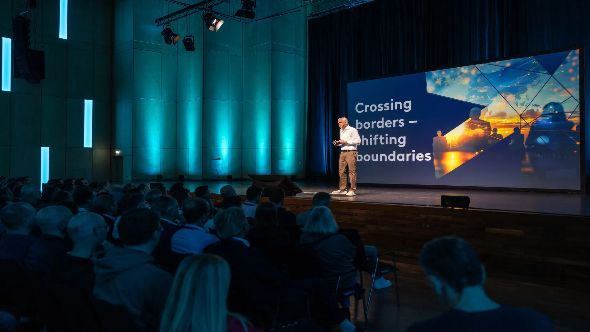 A man presenting on a stage in front of a crowd