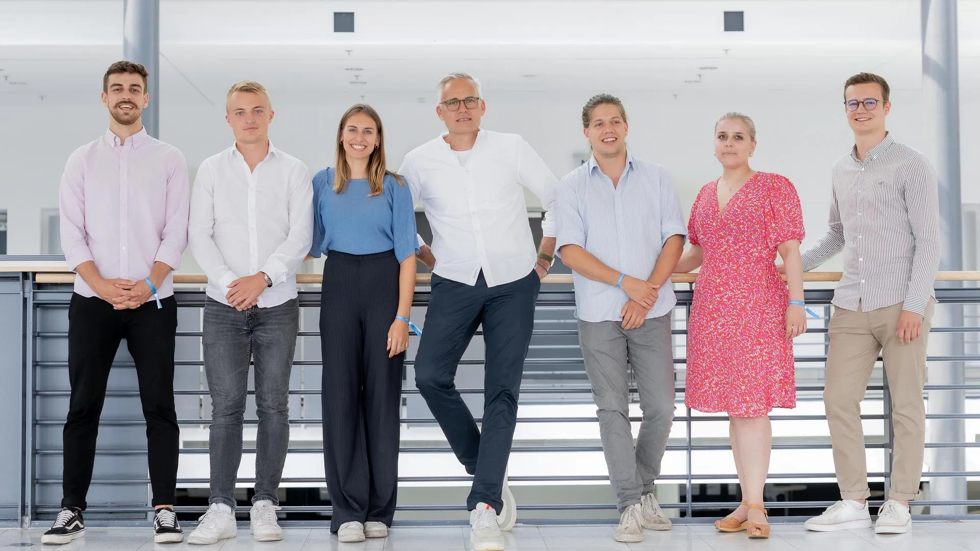 Eine Gruppe von Menschen lehnt an einem Geländer und lächelt in die Kamera.