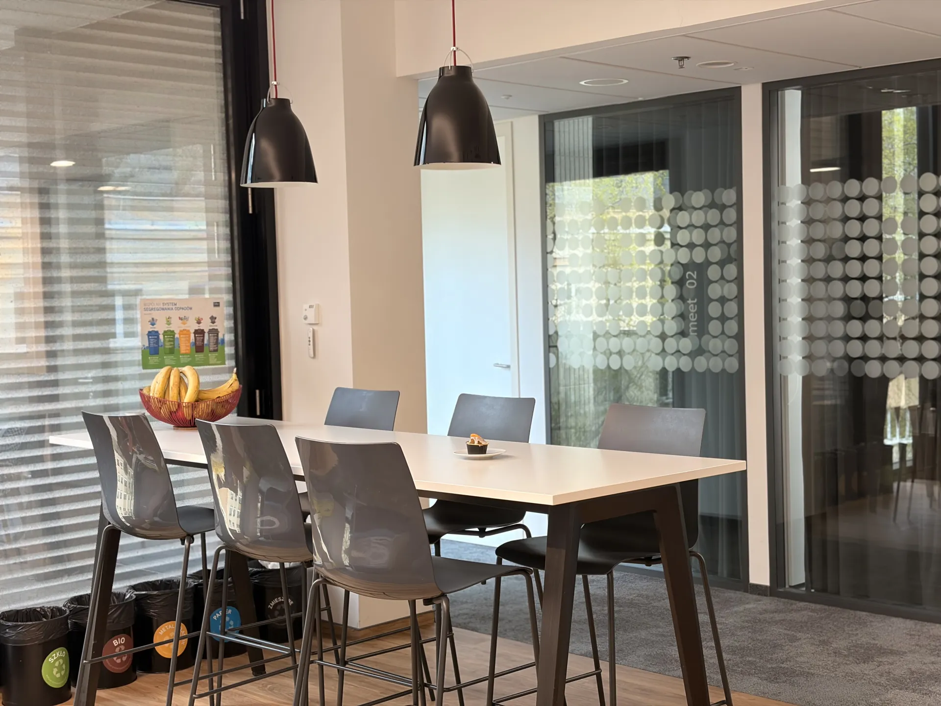 a table with chairs and a bowl of bananas in front of a glass wall