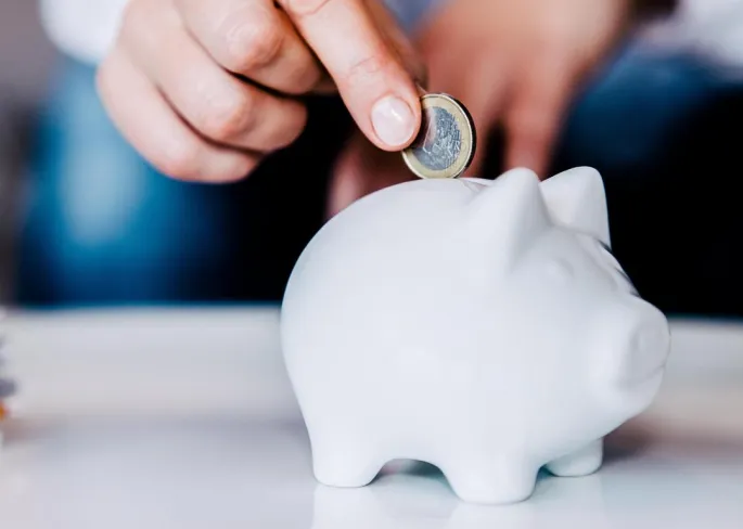 A person putting a coin into a white piggy bank