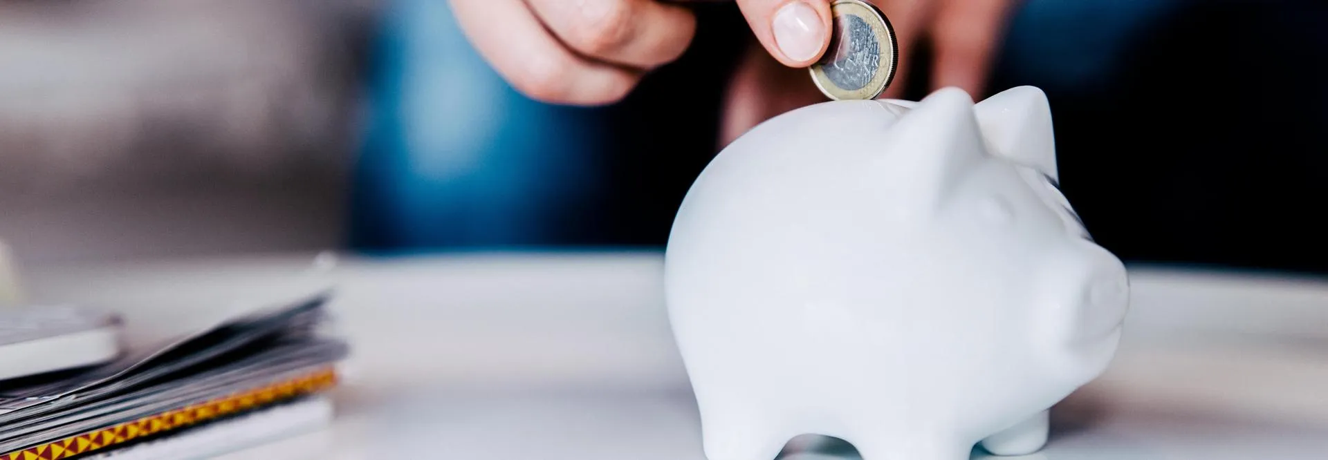 A hand is putting a coin into a piggy bank.