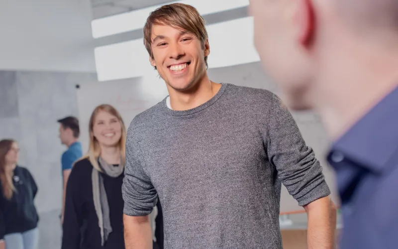 Ein Mann in einem grauen Pullover lächelt in die Kamera.