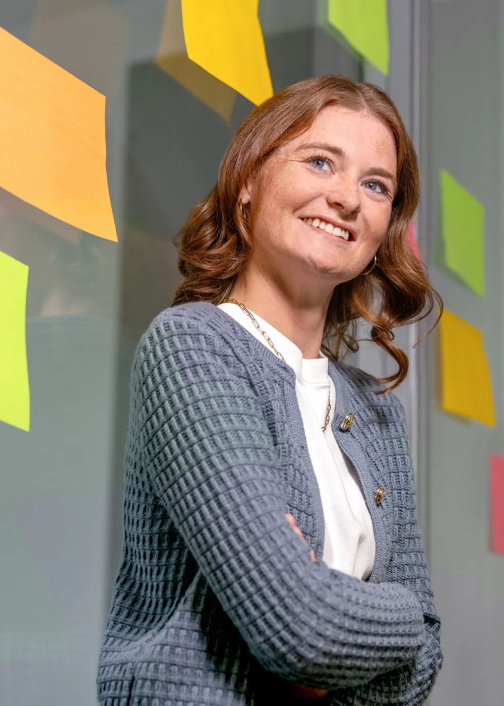 Eine Frau lächelt mit verschränkten Armen und gelben Post-its an einer Glaswand