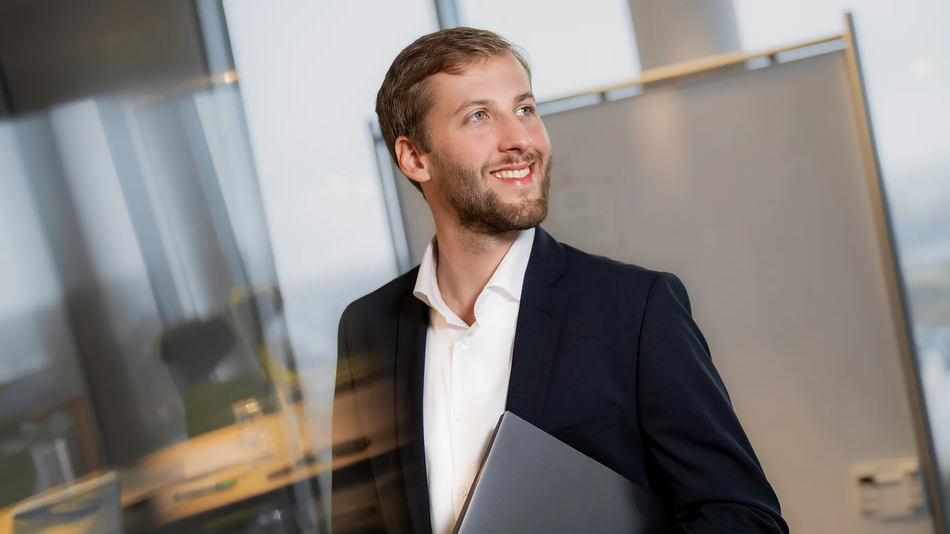 Ein Mitarbeiter von zeb hält einen Laptop unter dem Arm. Im Hintergrund befindet sich eine Tafel.